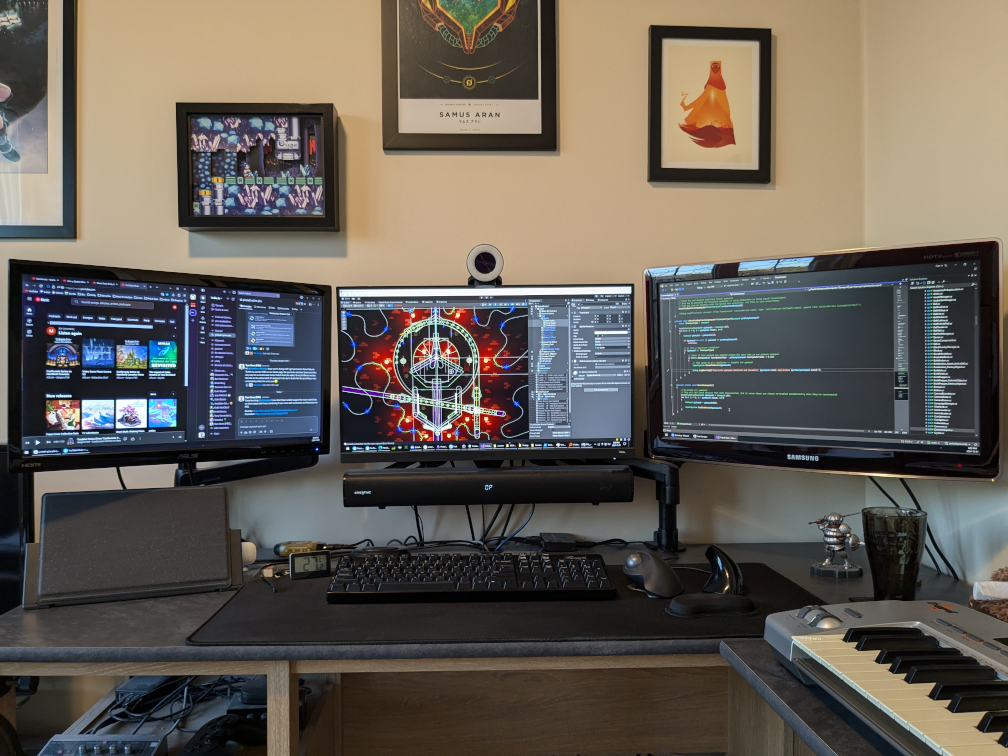 Tom Voros working desk featuring three screens. Behind are a few framed pictures on the wall.